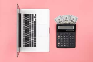 a calculator, laptop and money on a pink background